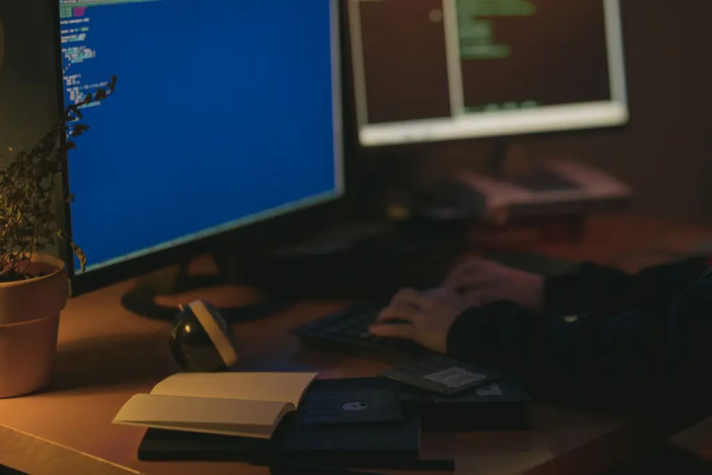 Developer integrating trade data, code on two screens in a dim office
