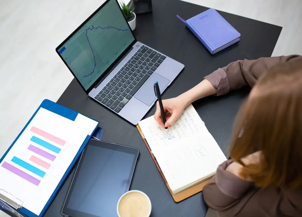 Analyst researching a company, notes beside a laptop with charts